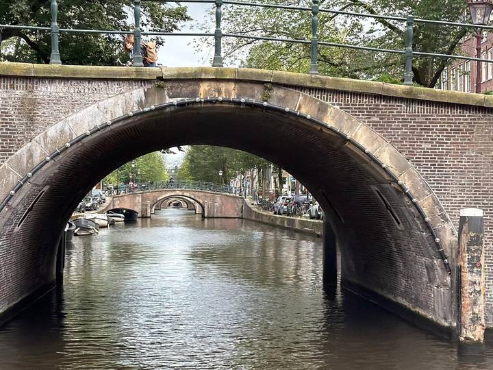 View through a brick arch bridge over a calm Amsterdam canal with more bridges in the distance.