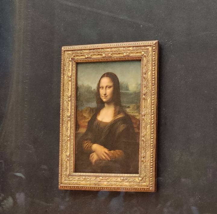 Photo of the Mona Lisa painting behind protective glass at the Louvre.