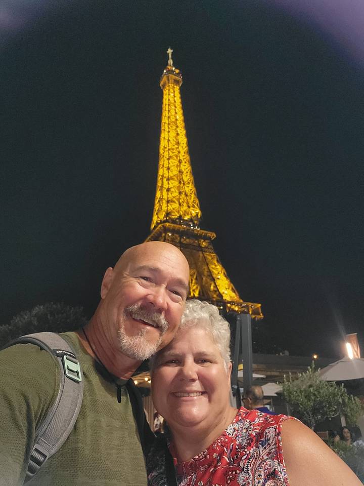 Night selfie of a couple in front of the illuminated Eiffel Tower.