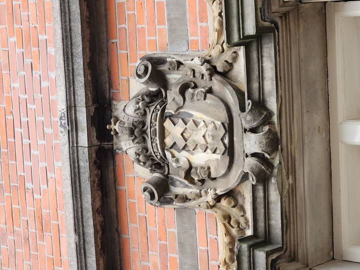 Stone coat of arms with triple X crest mounted on a red-brick Amsterdam building.