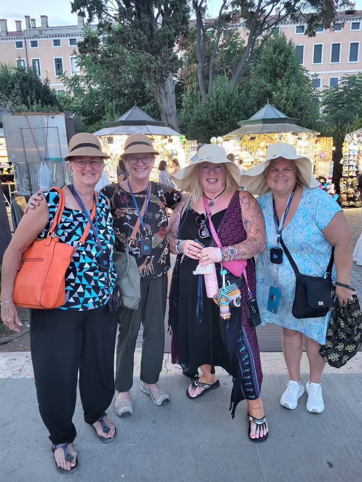 Four women wearing wide-brimmed hats smiling together at an outdoor fair.