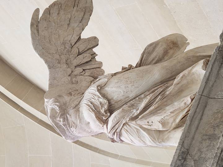 Marble statue of the Winged Victory of Samothrace viewed from below inside the Louvre.