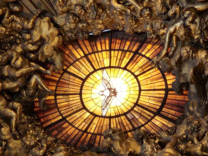 Radiant golden stained-glass window featuring a white dove surrounded by dramatic baroque sculpture inside a grand basilica.