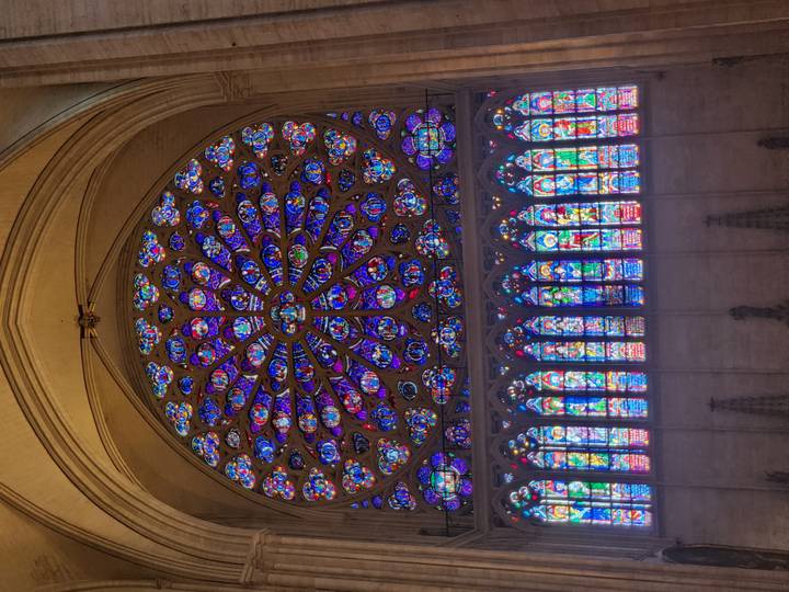 Vibrant rose window and rows of colourful stained-glass panels in a towering Gothic cathedral nave.