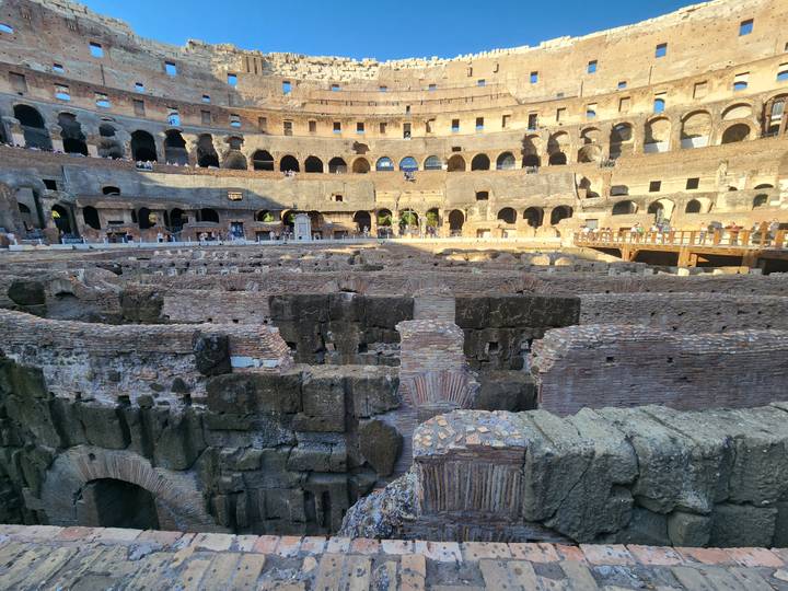 Stone terraces and hypogeum chambers inside the sun-lit arena of the Roman Colosseum.