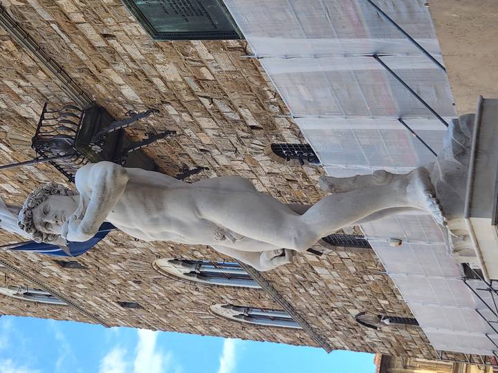 Marble replica of Michelangelo’s David standing before a rustic stone palace facade in Florence.