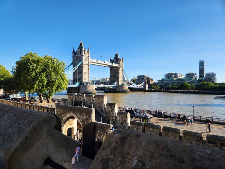 Tower Bridge spans the River Thames under clear blue skies, viewed from the ramparts of the Tower of London.