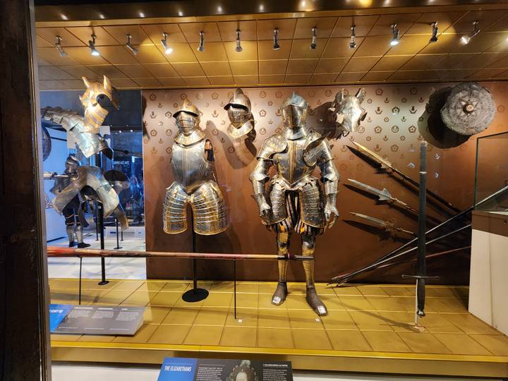 Display of medieval and renaissance suits of armour, helmets and polearms in a museum gallery.