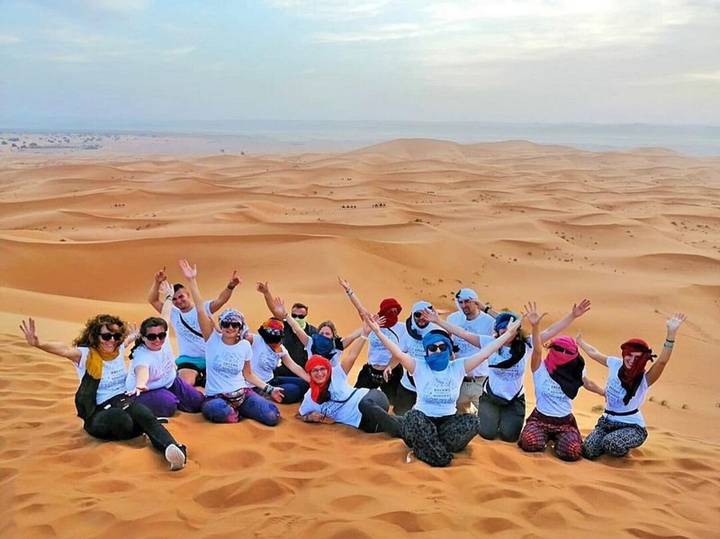 Large group of travelers celebrating atop a golden Sahara dune with vast sand sea behind