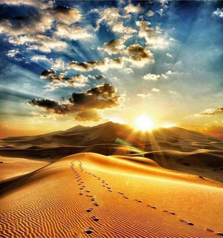 Golden sun breaking over Sahara dunes beneath a dramatic cloud-streaked sky