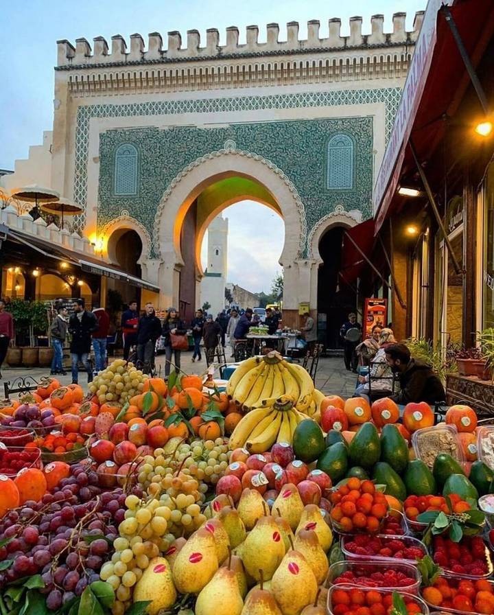 Colorful fruit stall in front of the Blue Gate with evening crowds in Fes