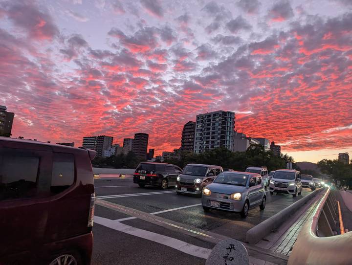Evening traffic crossing a bridge beneath dramatic red-pink clouded sky over cityscape