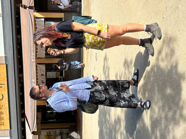 Two travelers enjoy ice cream outside a Japanese shop on a sunny day
