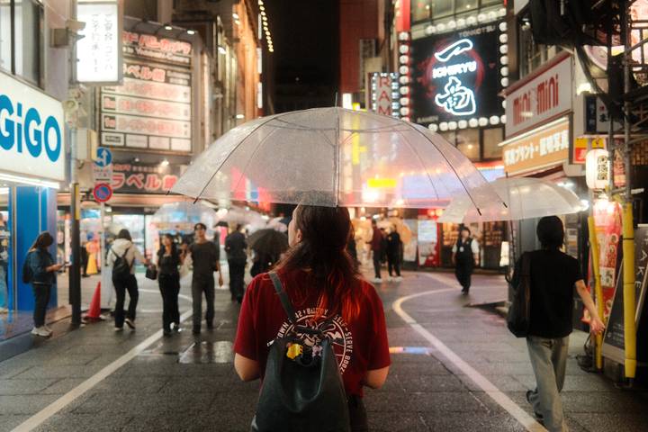 Night street scene in Japan with pedestrians and bright neon signs, subject holding clear umbrella in rain