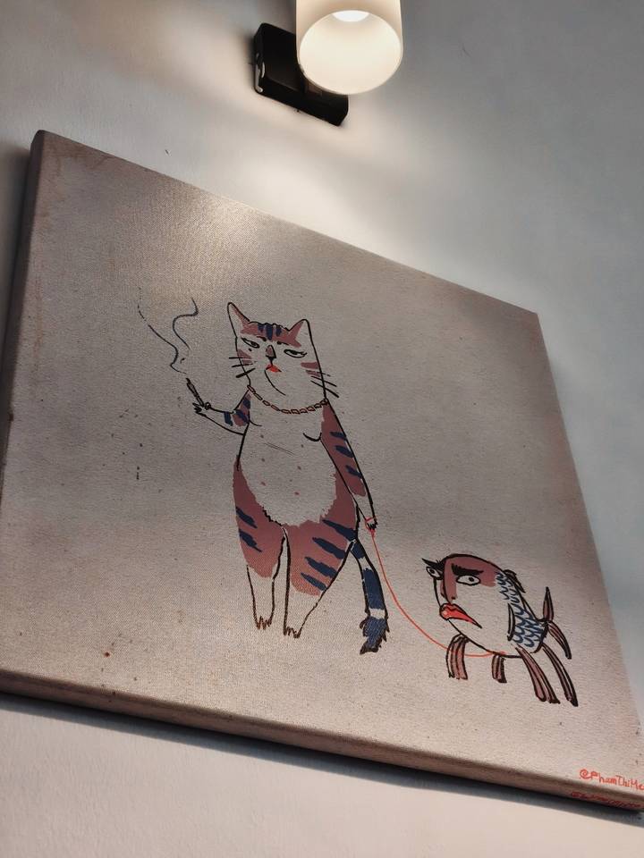 Close-up photograph of whimsical cat artwork smoking a cigarette on a wall canvas.