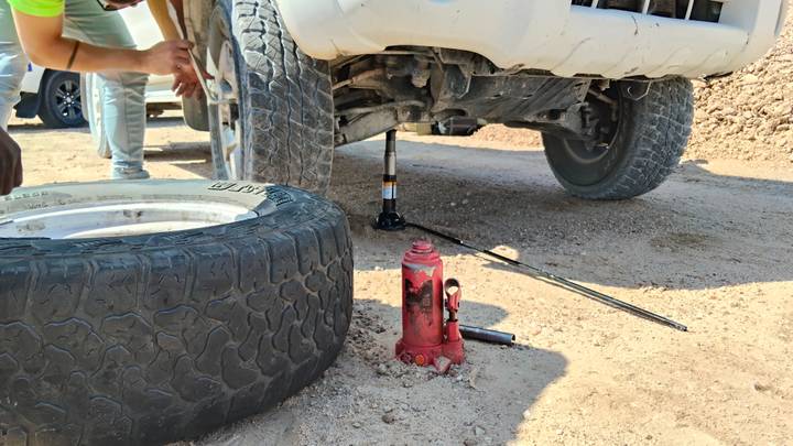 Mechanics changing a flat tyre on a 4x4 in a dusty desert setting.