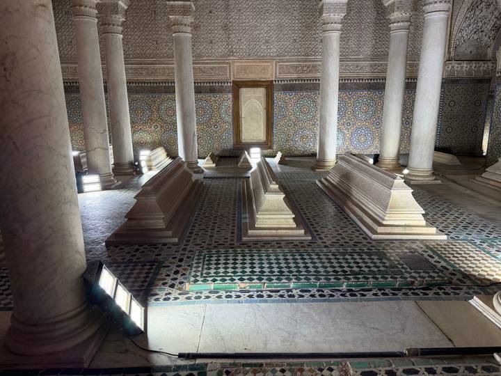 Ornate interior hall with marble tombs, mosaic walls and slender columns in soft light.