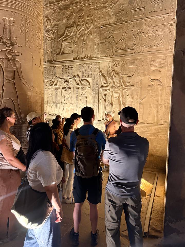 Guide explaining wall carvings inside an ancient Egyptian temple to interested travellers.