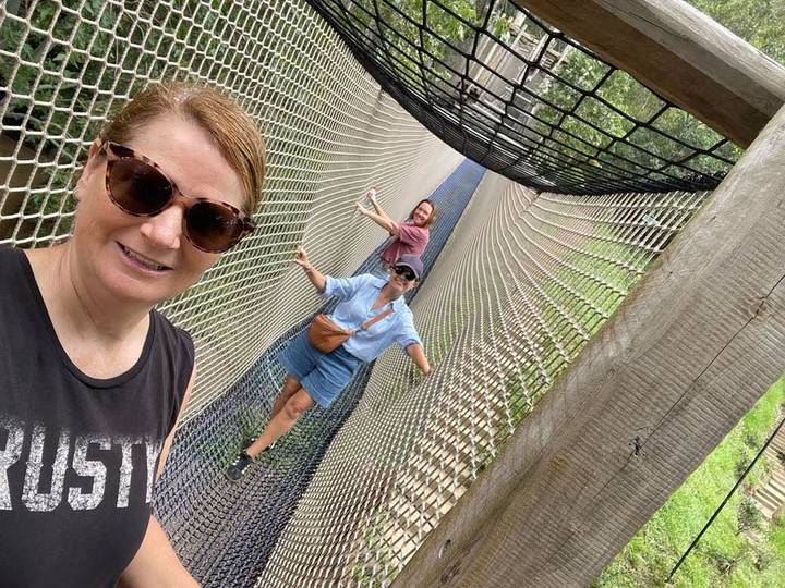 Three friends balancing on a high rope bridge and taking a selfie.