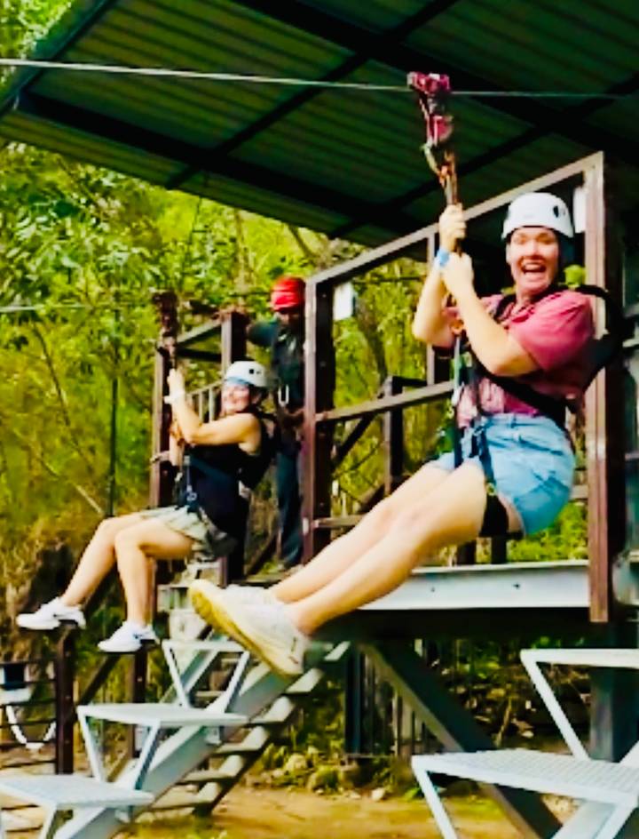 Motion-blurred shot of two people zip-lining through trees.