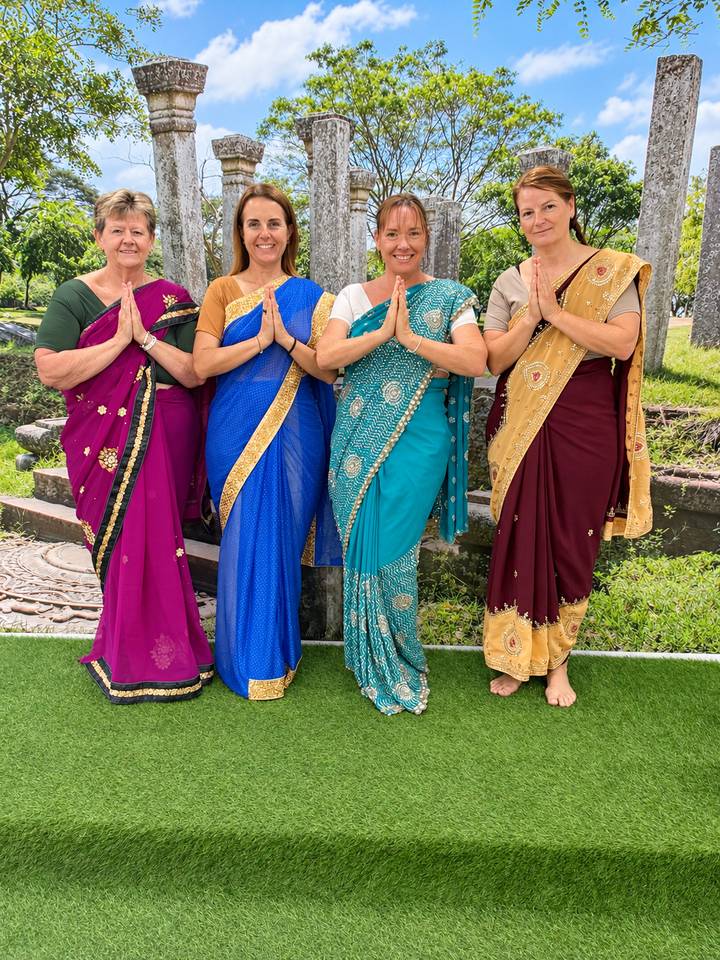 Women dressed in colourful saris posing with traditional greeting gesture.