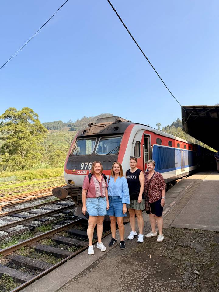 Travellers posing beside a colourful hill-country train at a rural station.