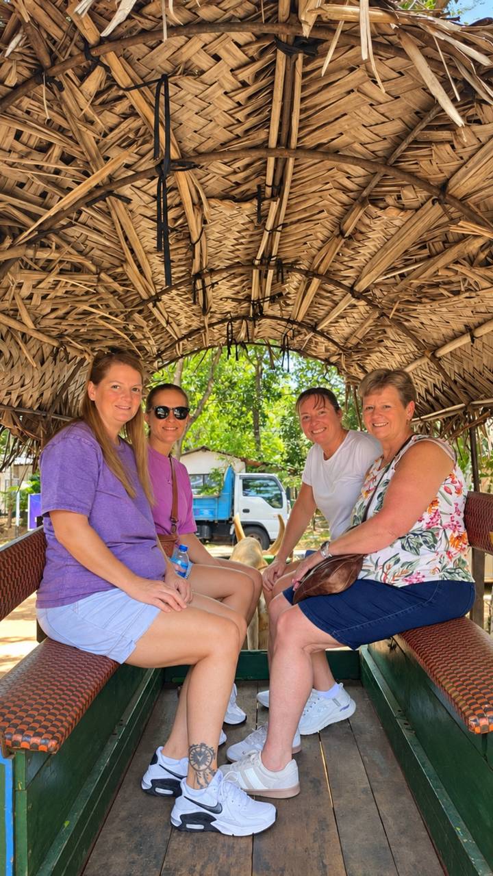 Four women seated inside a thatched cart with greenery in the background.