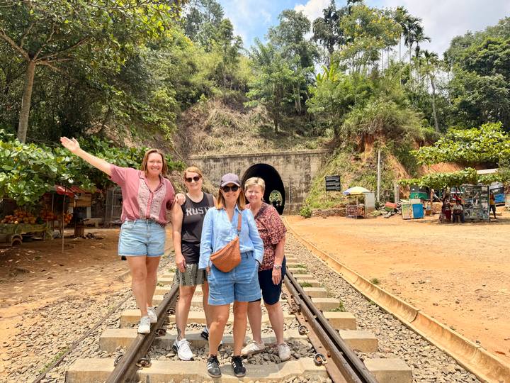 Travellers balancing on railway tracks near the entrance of a tunnel in the jungle.