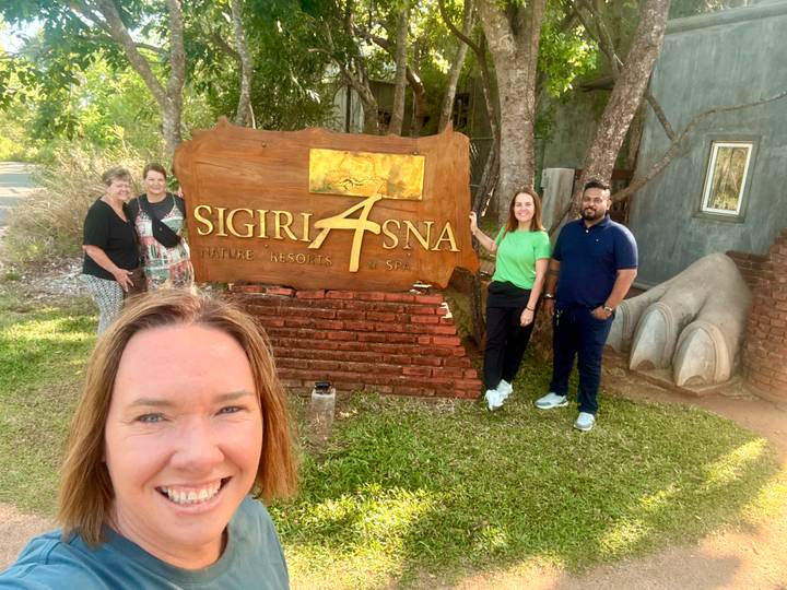 Selfie of travellers beside the wooden Sigiriya Asna resort sign.