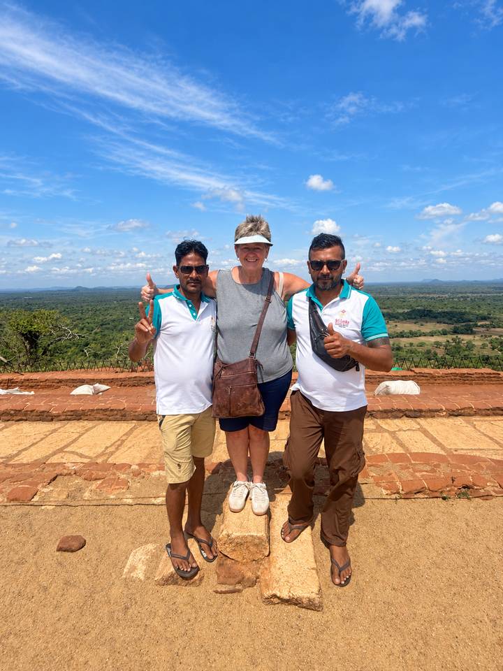 Tourist flanked by two local guides posing on a hill-top viewpoint with plains below.