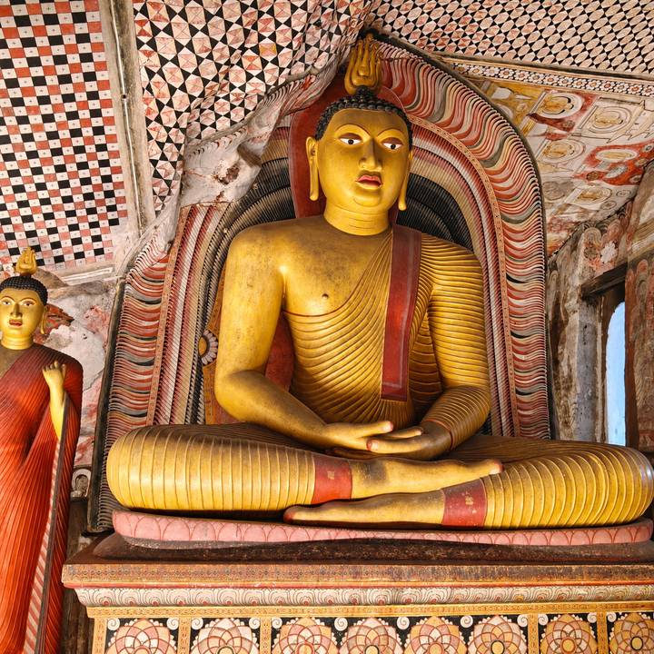 Close-up of a golden seated Buddha statue inside an ornately painted cave temple alcove.