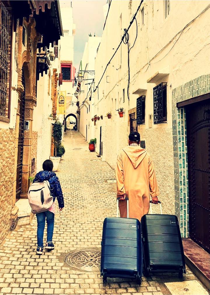 Man and child walking through narrow white-washed alley with hanging flower pots in a medina.