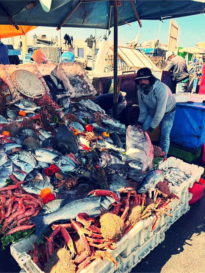Vendor arranging a large, colorful pile of fresh fish and seafood at an outdoor market stall.