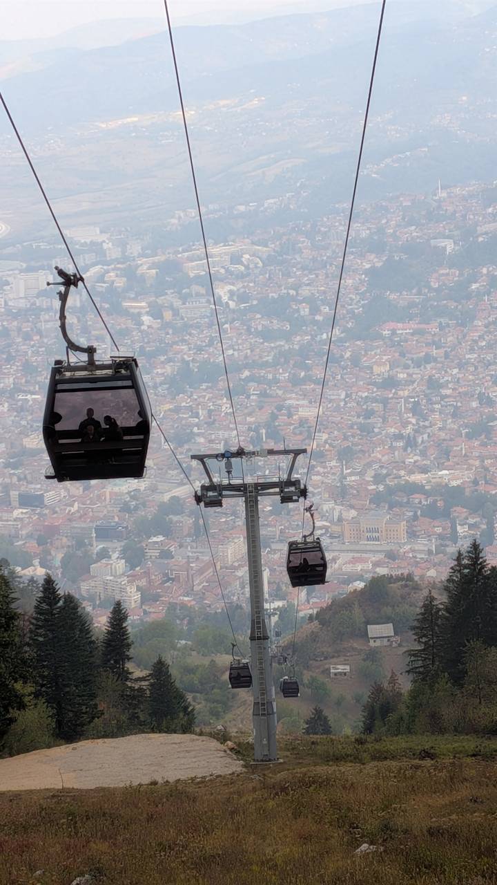 Cable cars ascending above Sarajevo with hazy cityscape spread out far below.