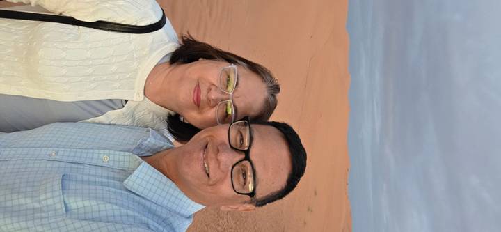 Couple smiles in the soft light of dawn standing among smooth orange dunes of the Sahara.