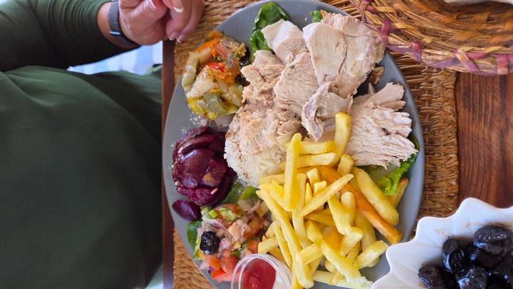 Plate of fries, sliced chicken and assorted Moroccan salads served on a woven place mat.