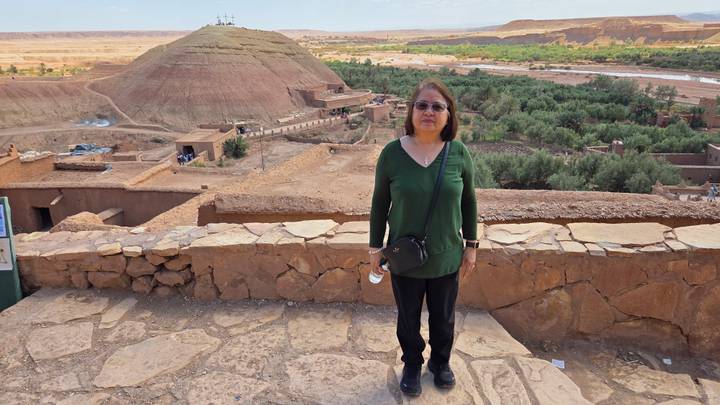 Traveler stands at viewpoint overlooking green oasis and desert hill topped with crosses near Ait Benhaddou.