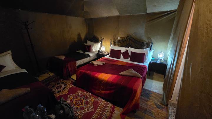 Interior of desert tent accommodation with double and single beds, patterned rugs and lantern lighting.