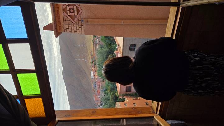 Back view of woman looking out colourful framed window toward mountain town and antenna masts.