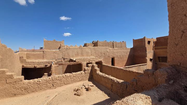 Crumbling adobe structures and high walls of an abandoned desert village under clear blue sky.