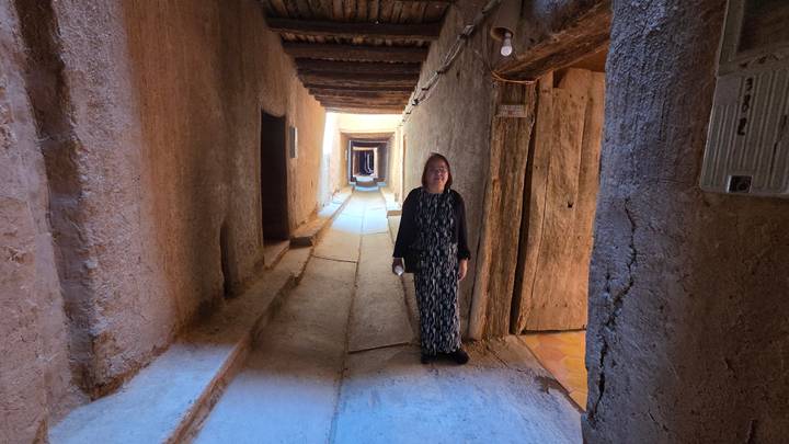 Traveller walking through narrow covered adobe passageway with wooden beams overhead.