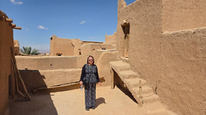 Traveller standing among earthen adobe buildings and stairs under bright blue sky.