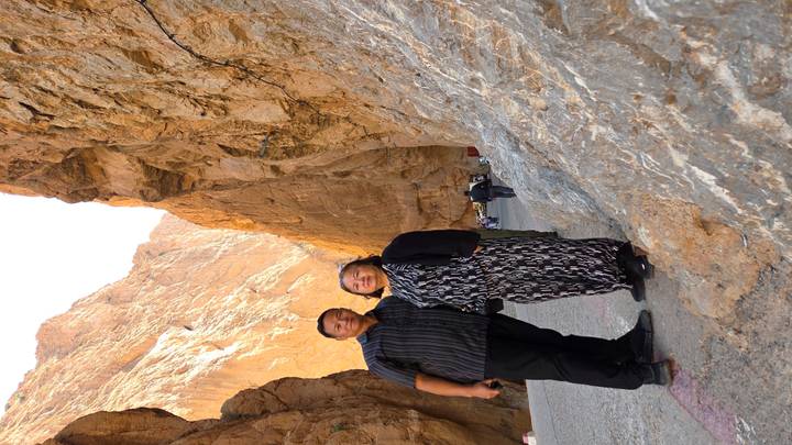 Couple posing together beside steep canyon walls on paved road.