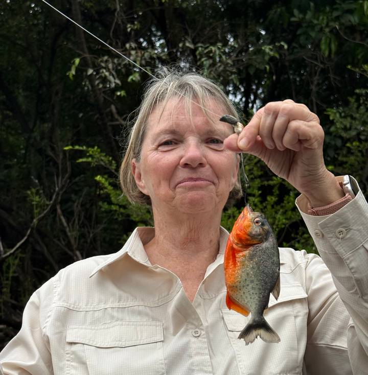 Traveller proudly holding up freshly caught piranha fish in Amazon setting.
