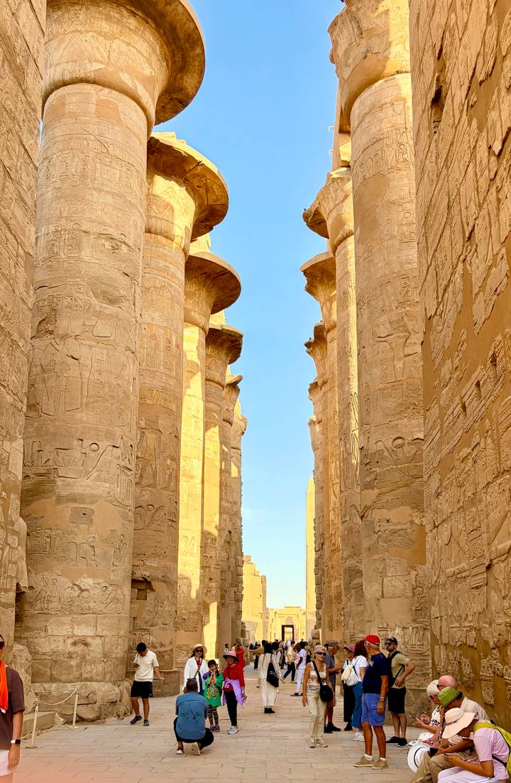 Massive ancient columns filled with hieroglyphs reach toward a bright blue sky.