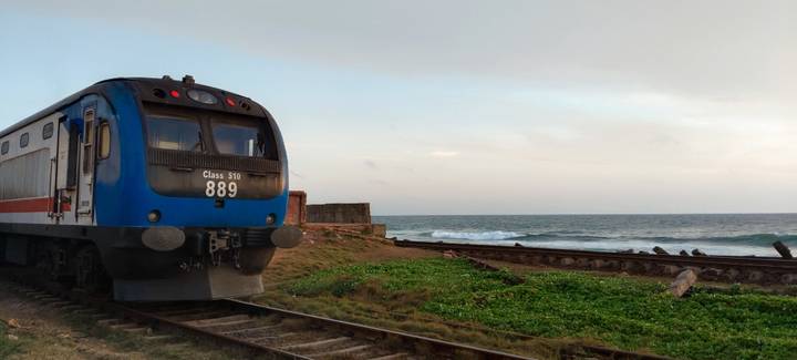 Blue coastal train carriage parked beside railway tracks that run right along the ocean shore