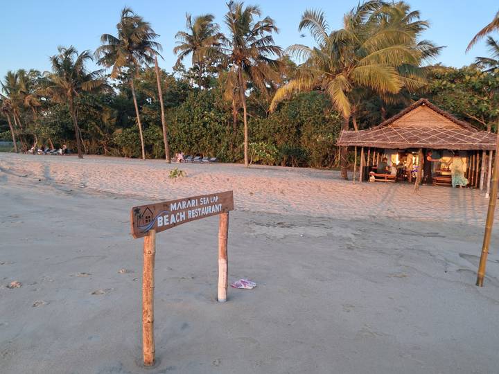 Quiet sandy beach at sunset with simple thatched beach shack and sign for a seaside restaurant