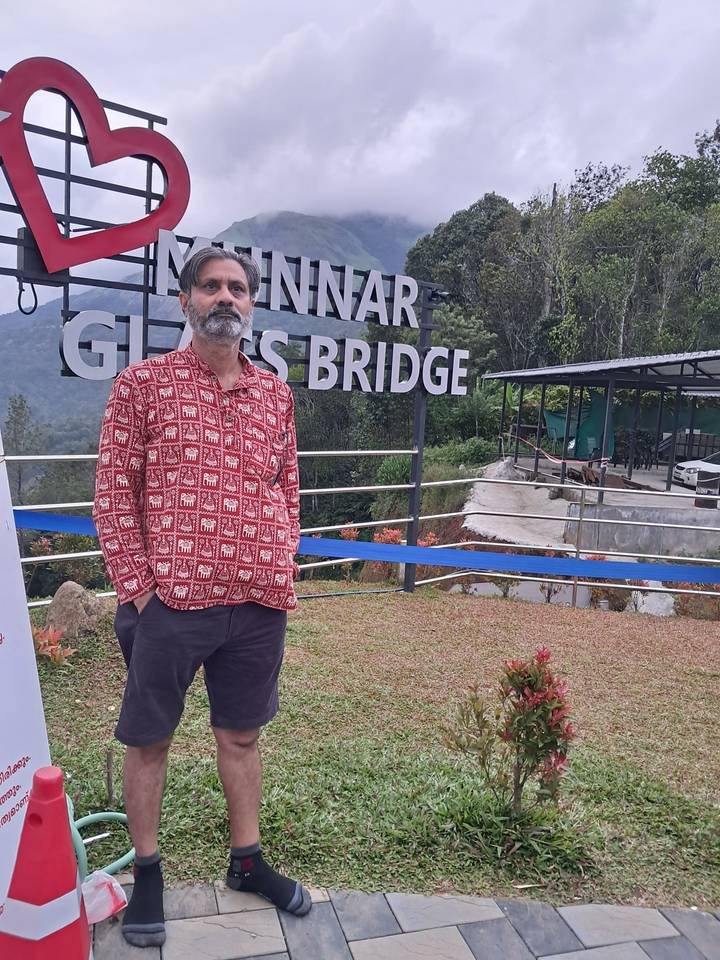 Man posing in front of the Munnar Glass Bridge viewpoint with misty hills behind