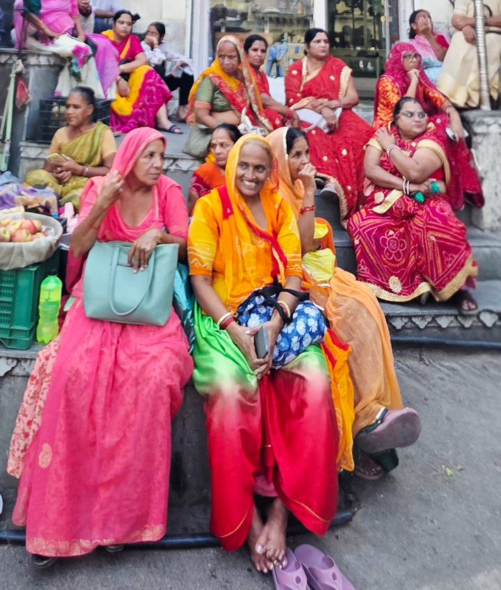 Women in vibrant Rajasthani dress resting on market steps with baskets of produce