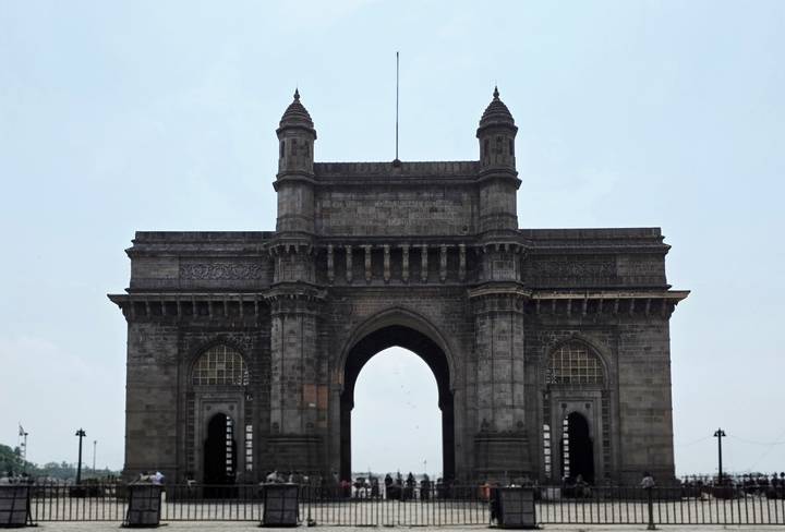 Monumental basalt Gateway of India arch standing against a pale sky in Mumbai